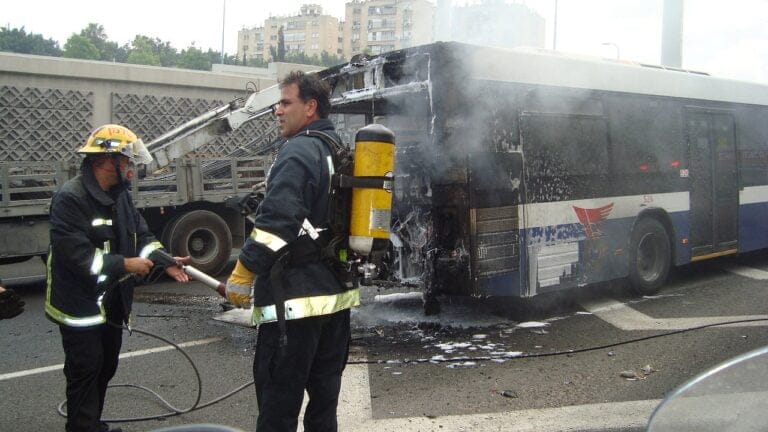 Firefighters extinguishing a burning bus on road.