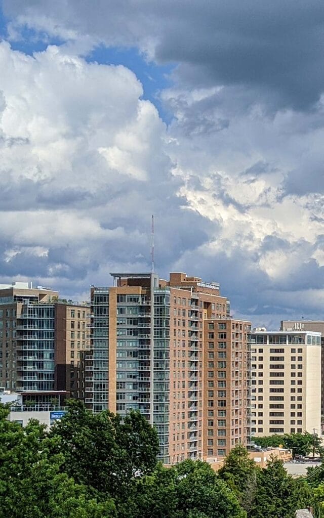 City buildings under cloudy sky, with green trees.