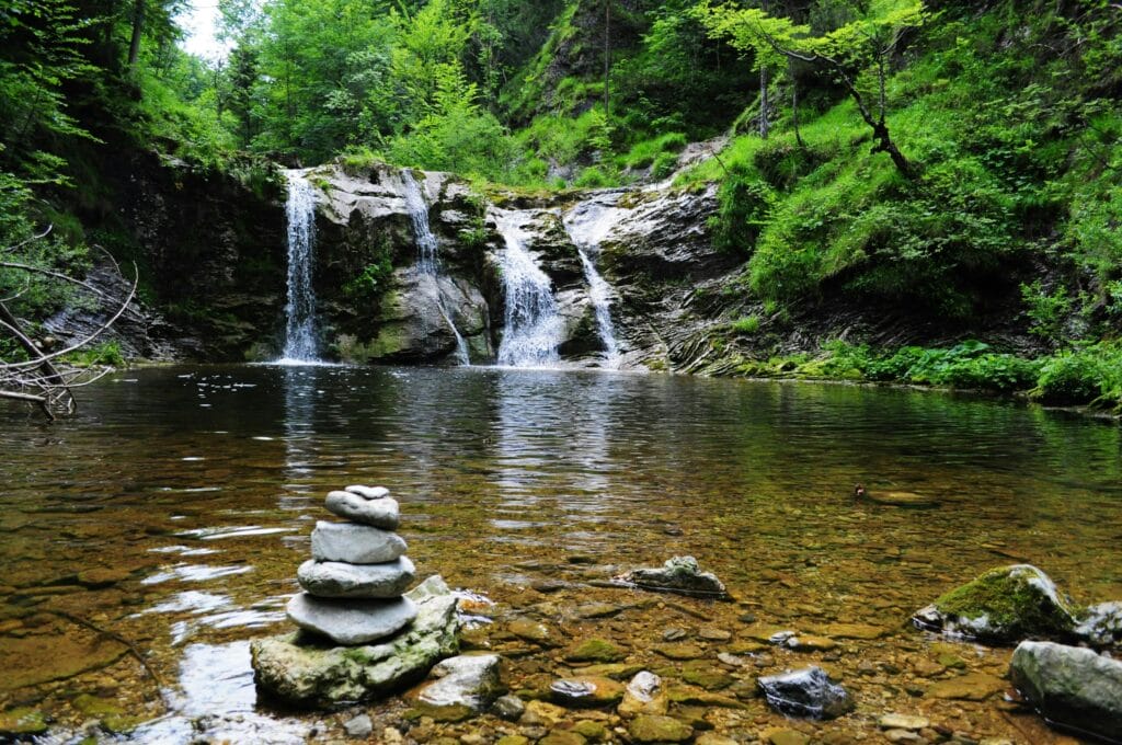 Peaceful forest waterfall with serene stone cairn, ideal for nature and travel themes.